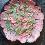 Rucola en pijnboompitten over de rosbief verdelen en het citroensap en de olijfolie erover heen schenken