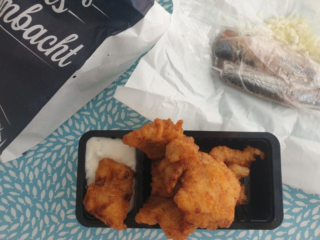 Tafel met portie kibbeling met saus en harinkjes in de achtergrond