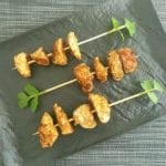 Zwarte schaal met kipspiesjes en koranderblaadjes