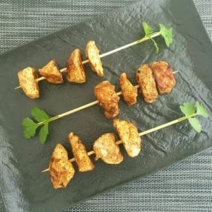 Zwarte schaal met kipspiesjes en koranderblaadjes