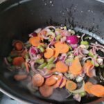 Grote braadpan met stukjes wortel, rode ui en bleekselderij op matig-laag vuur